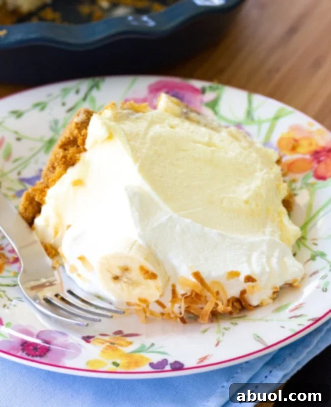 A close-up shot of a single slice of banana cream pie on a white plate, showcasing its layers.