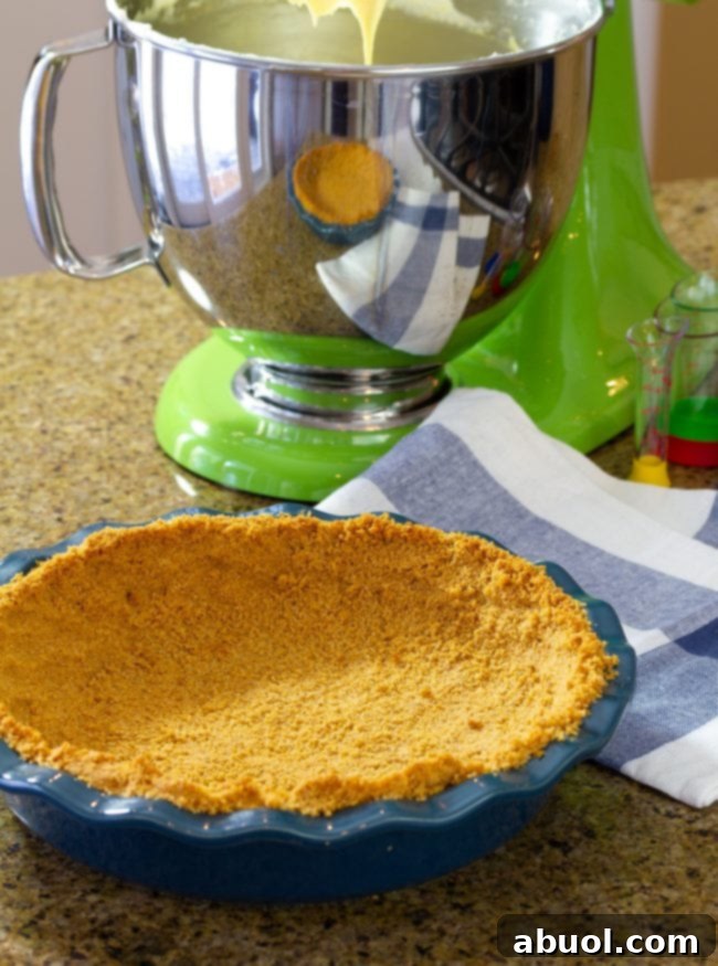 Graham Cracker Crust mixture in a pie dish, with a stand mixer in the background, ready to be pressed.