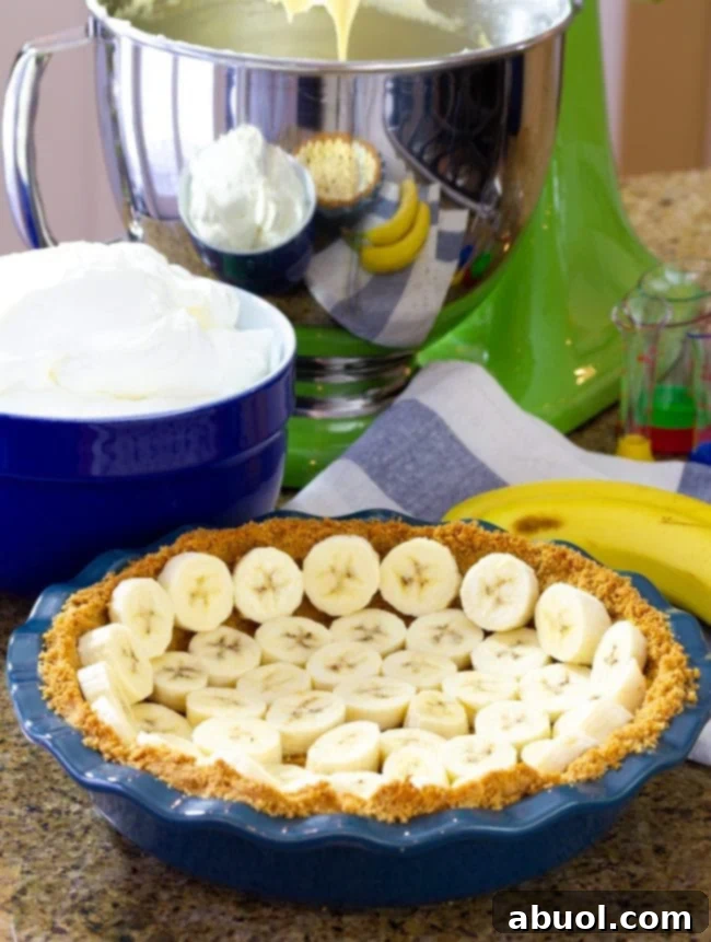 Adding fresh sliced banana slices to a baked graham cracker crust pressed into a blue pie plate.