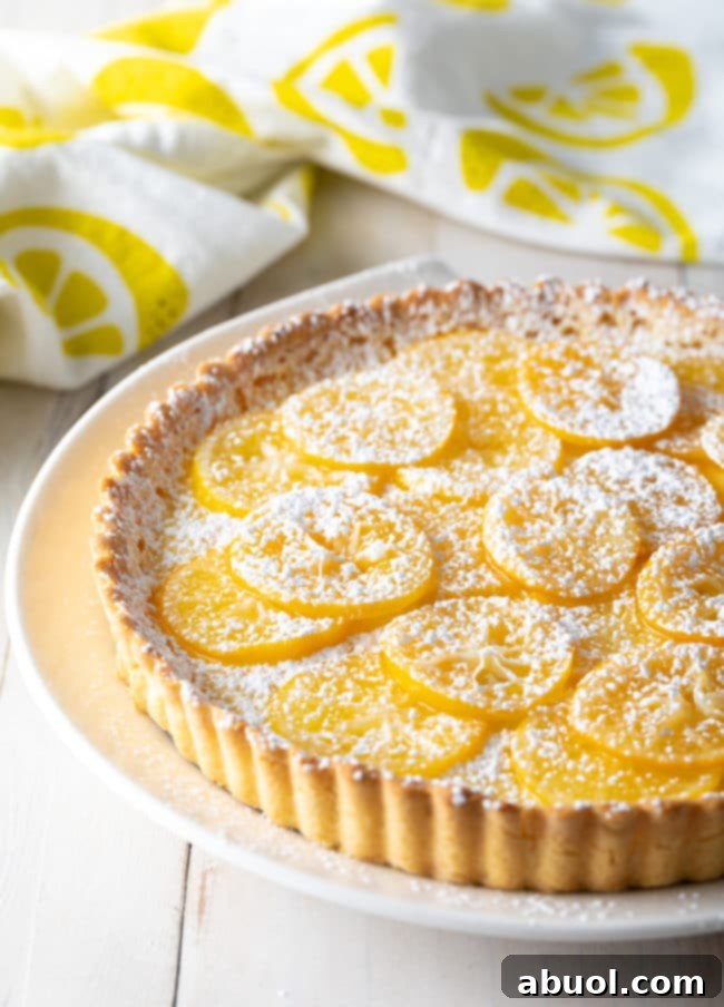 Easy Meyer Lemon Tart Recipe  - whole tart on plate, side angle, with lemon slices on top.