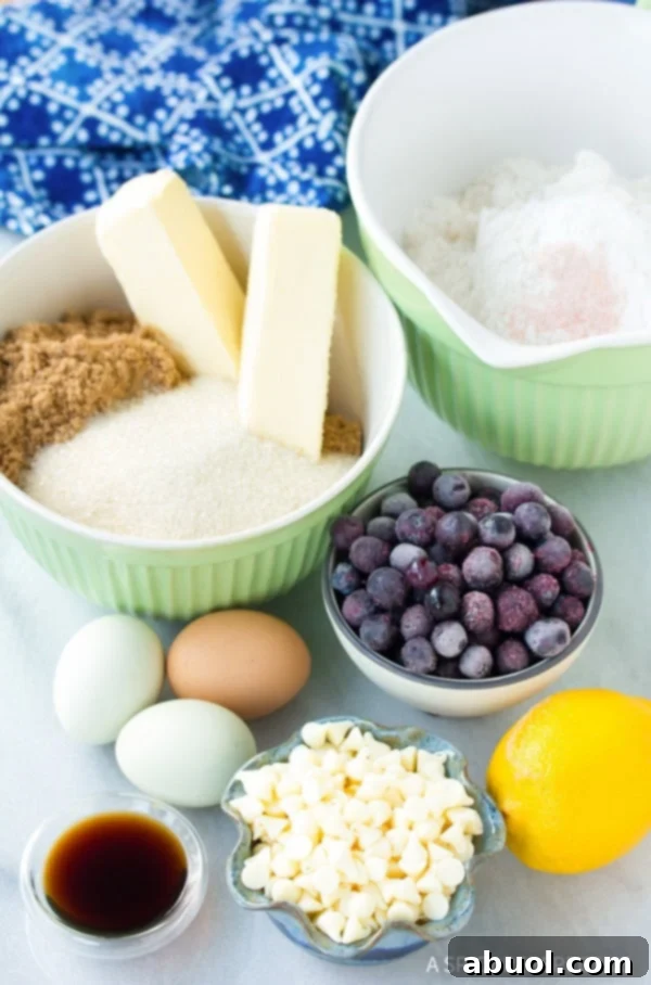 Green mixing bowl filled with flour. Green mixing bowl filled with 2 sticks of butter, brown sugar, and granulated sugar. 3 eggs and 1 lemon. Bowl filled with blueberries, bowl filled with white chocolate chips, and bowl filled with vanilla extract.
