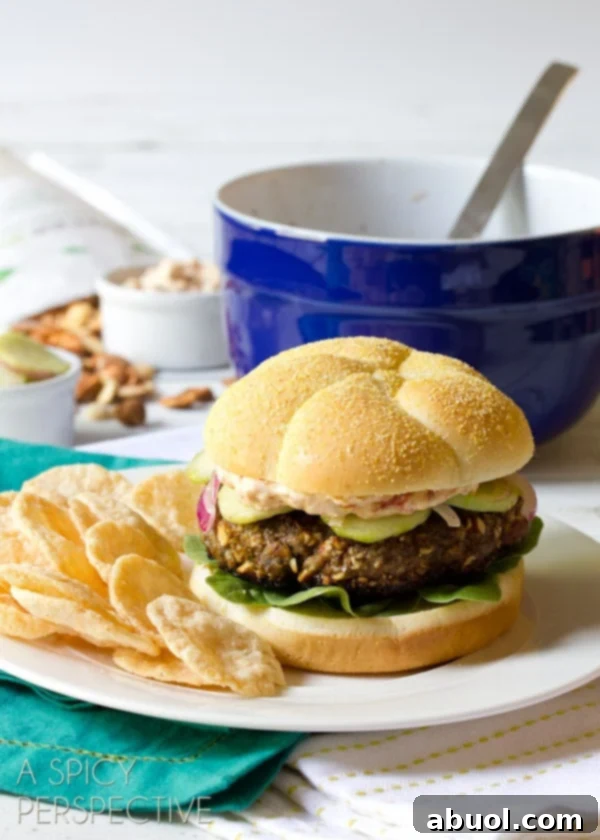 A detailed close-up of a plated Mediterranean burger, showcasing its intricate layers and appealing textures with chips in the background.