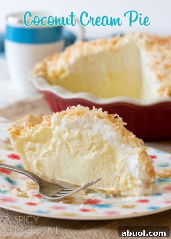 A delectable slice of Coconut Cream Pie rests on a plate, showcasing its pristine white, creamy filling, topped with a cloud of whipped cream and golden toasted coconut flakes.