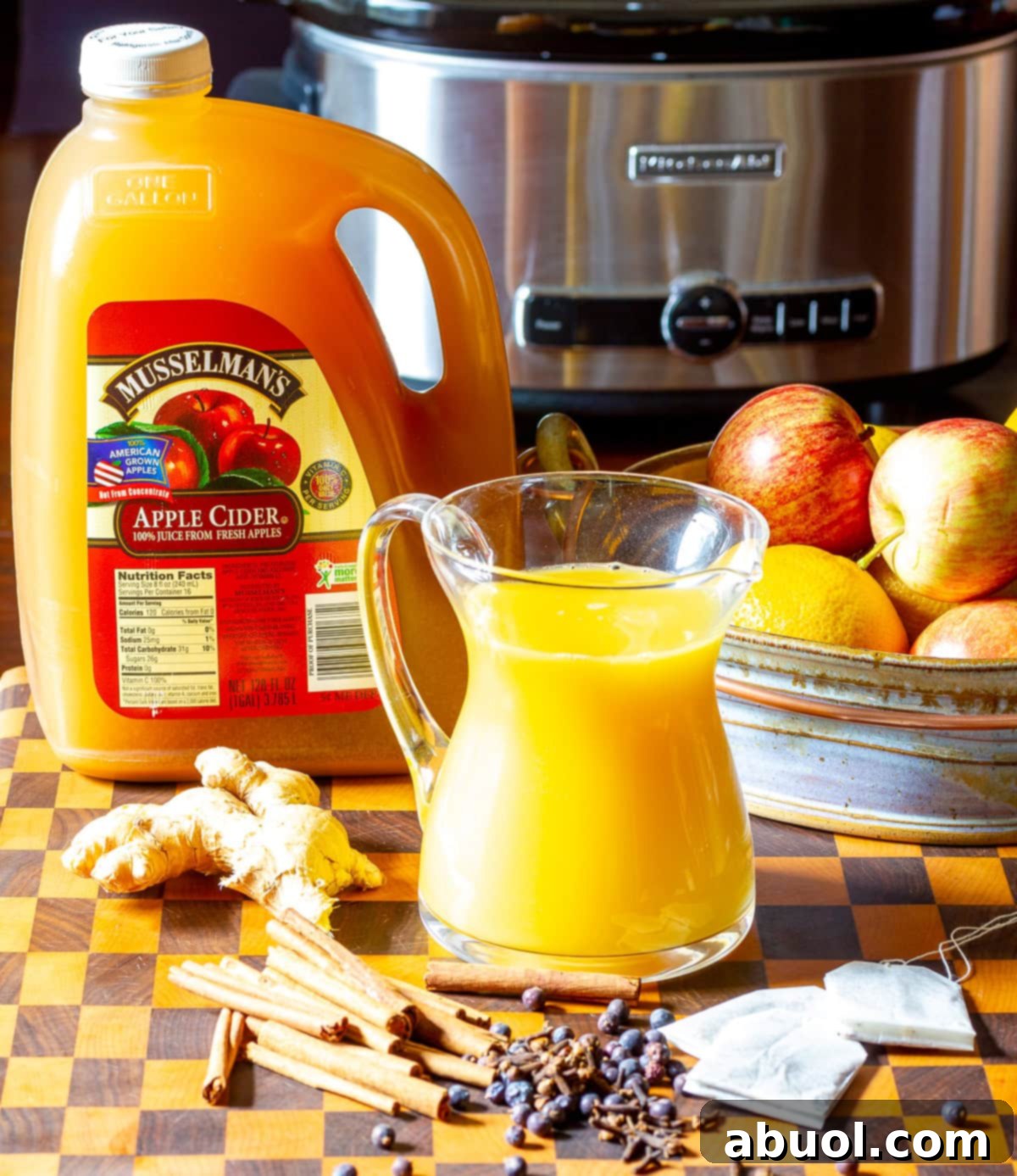 Essential ingredients arranged neatly, ready for making wassail, with a slow cooker in the background.