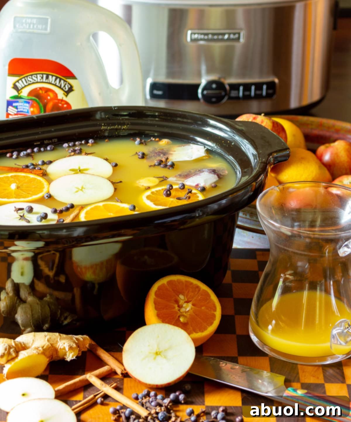 Close-up of apple cider wassail simmering in a crock pot, surrounded by fresh ingredients like apples, oranges, and spices.