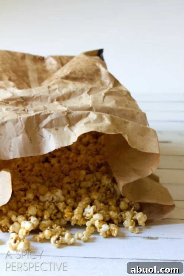 A rustic brown paper bag generously filled with golden, glistening caramel popcorn, showcasing its appealing texture and rich color.