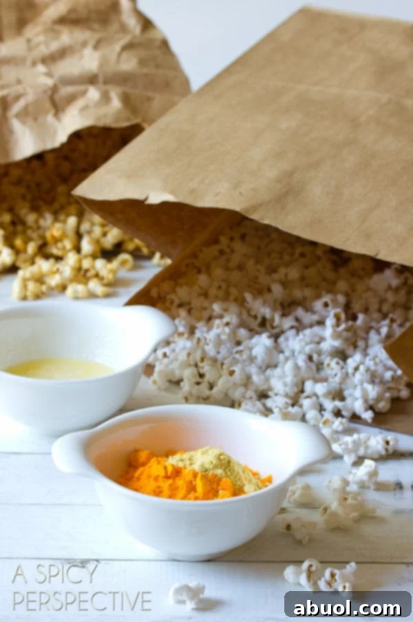 A focused shot of two paper bags of plain popped popcorn, positioned behind a bowl of melted butter and a small bowl of vibrant orange cheese powder, ready for their cheesy transformation.