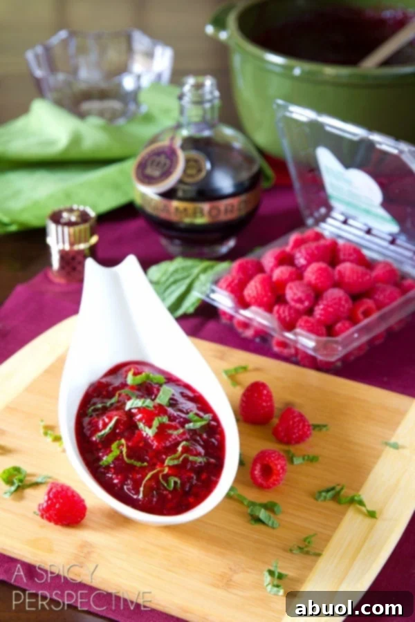 A small gravy boat filled with vibrant homemade cranberry raspberry sauce, garnished with fresh mint, ready to be served at a festive meal.