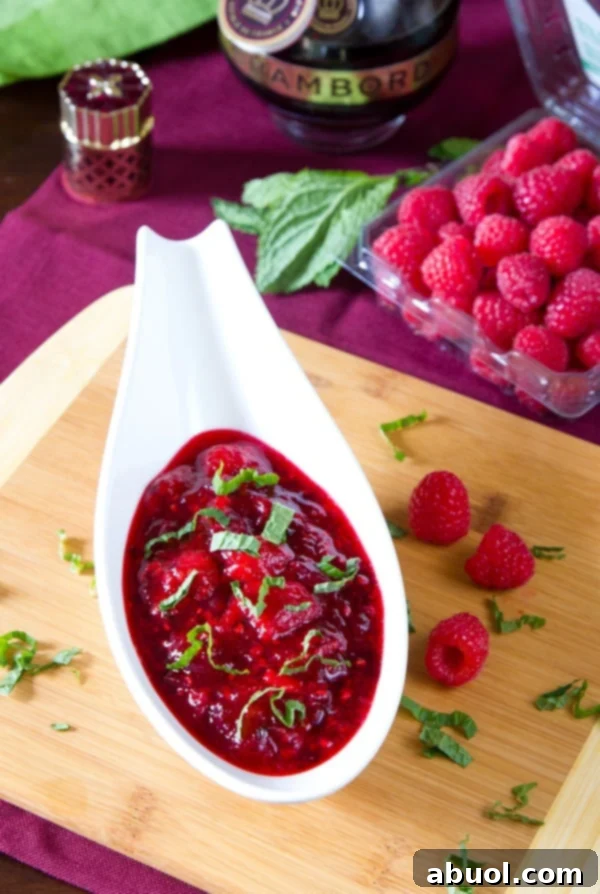 A small, elegant dish of homemade cranberry raspberry sauce, adorned with fresh mint and berries, perfect for a holiday meal or appetizer spread.