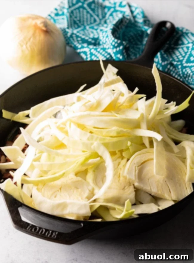 Adding sliced cabbage to the skillet with bacon
