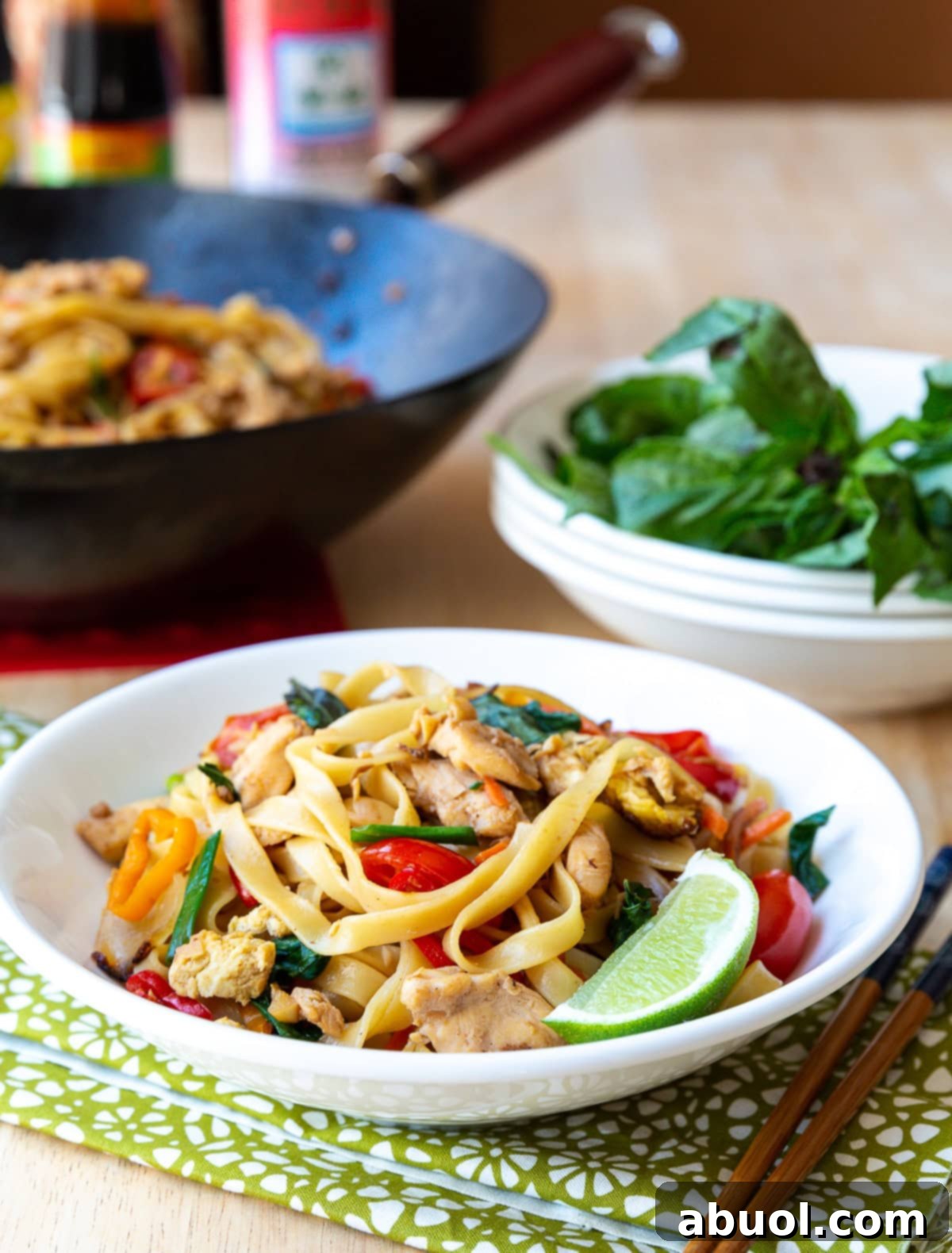 A close-up shot of Drunken Noodles in a white bowl, garnished with a lime wedge, with a pair of chopsticks resting on the side, ready to be enjoyed.