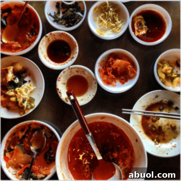 A vibrant spread of half-empty white bowls showcasing classic Korean side dishes, indicating a delicious meal has just been enjoyed.