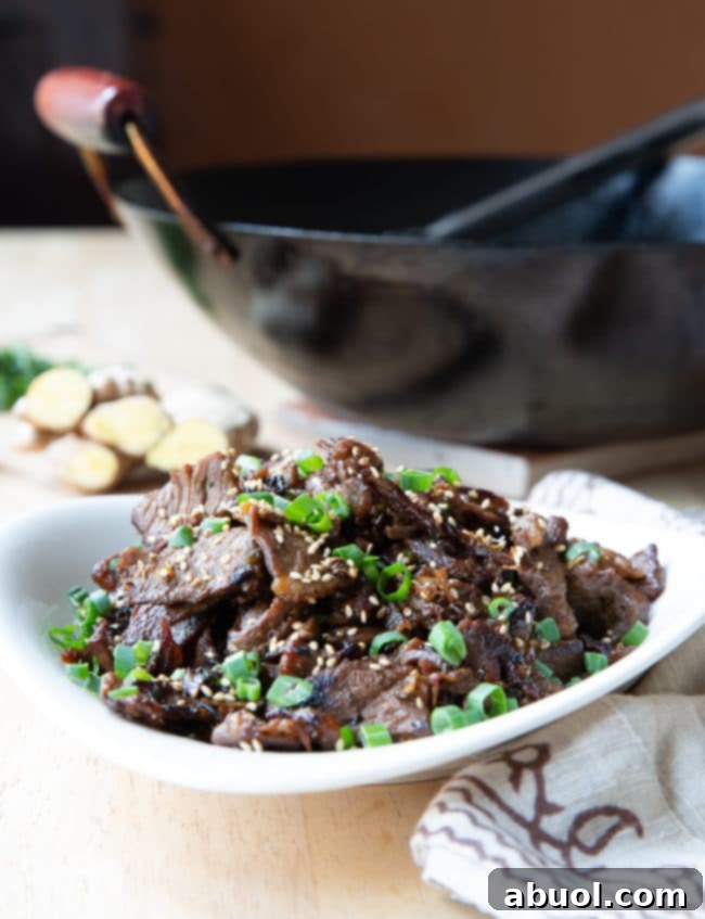 A bowl of freshly cooked Korean beef bulgogi, with a black wok blurred in the background, ready to be served.