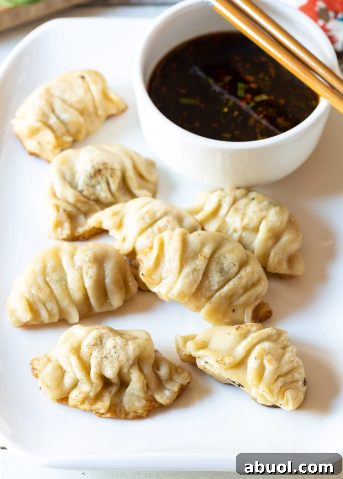 Potstickers served on a white plate next to a small bowl of dipping sauce.
