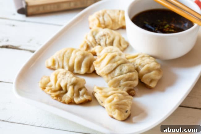 Dumplings on a plate with a bowl of sauce next to them.