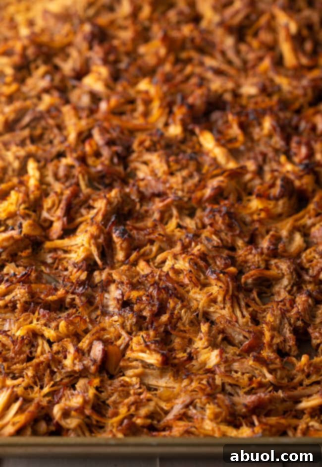 Broiled shredded carnitas on a baking sheet, featuring perfectly crispy, darkened edges.