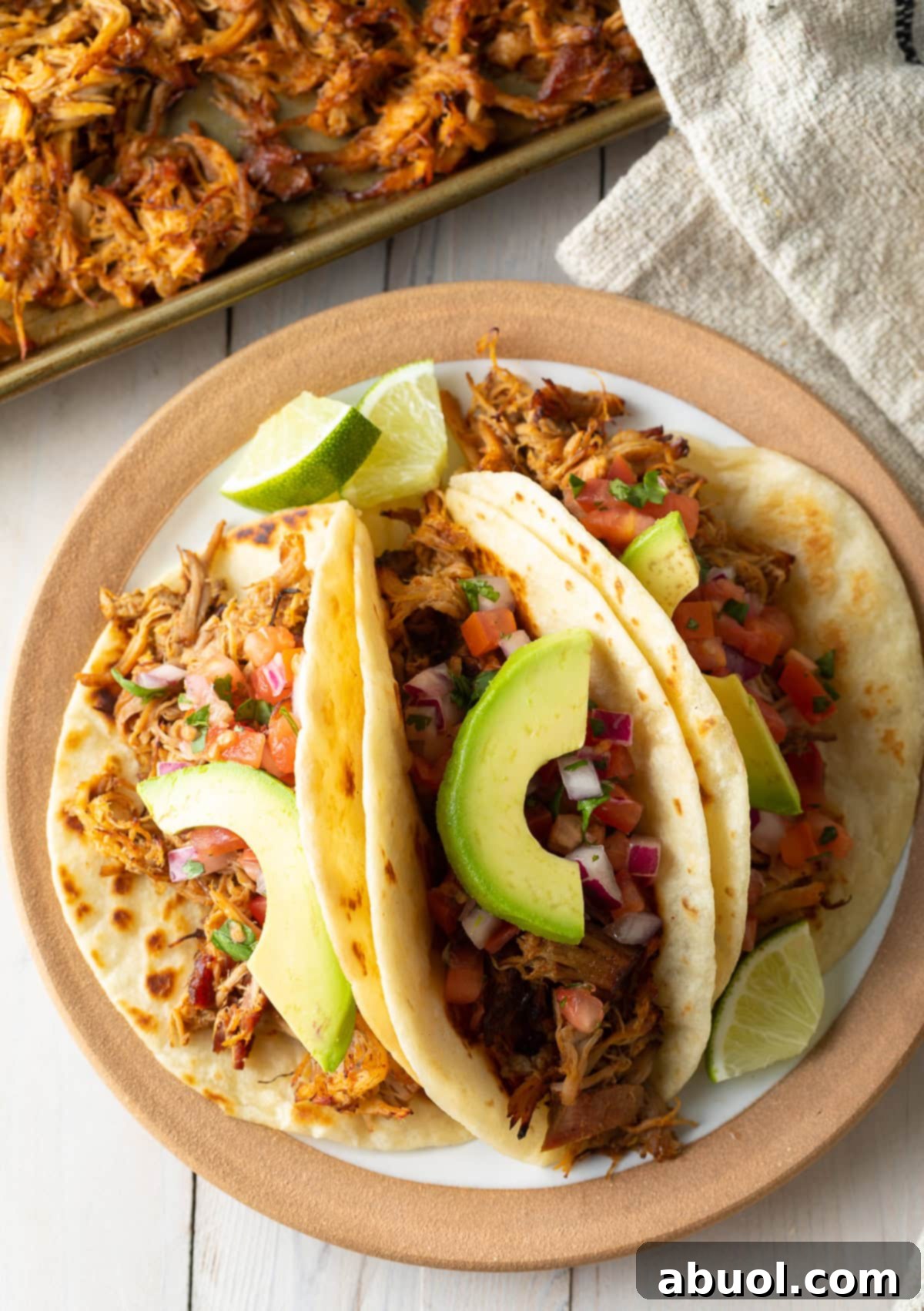 Overhead shot of three perfectly plated carnitas tacos adorned with avocado slices and fresh cilantro.