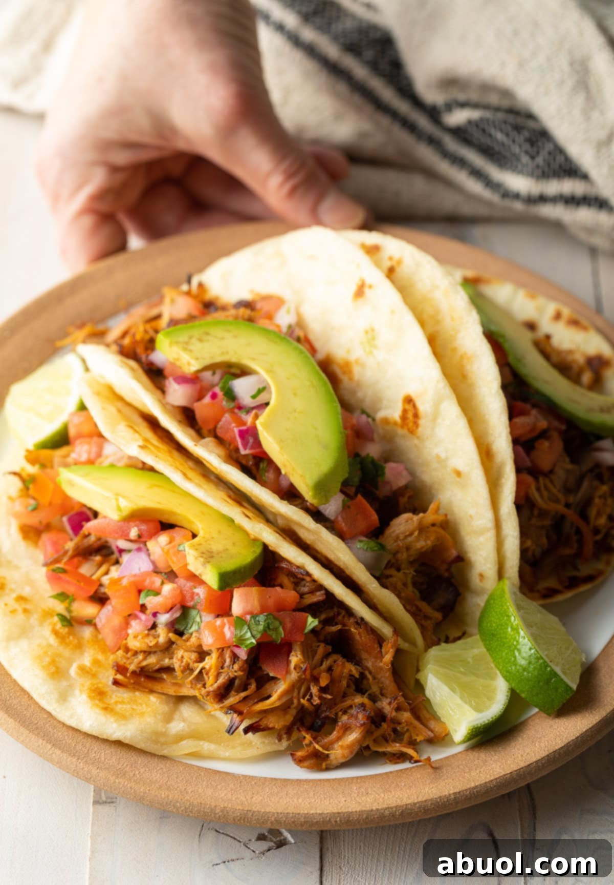 A hand holding a plate piled high with crispy carnitas tacos.