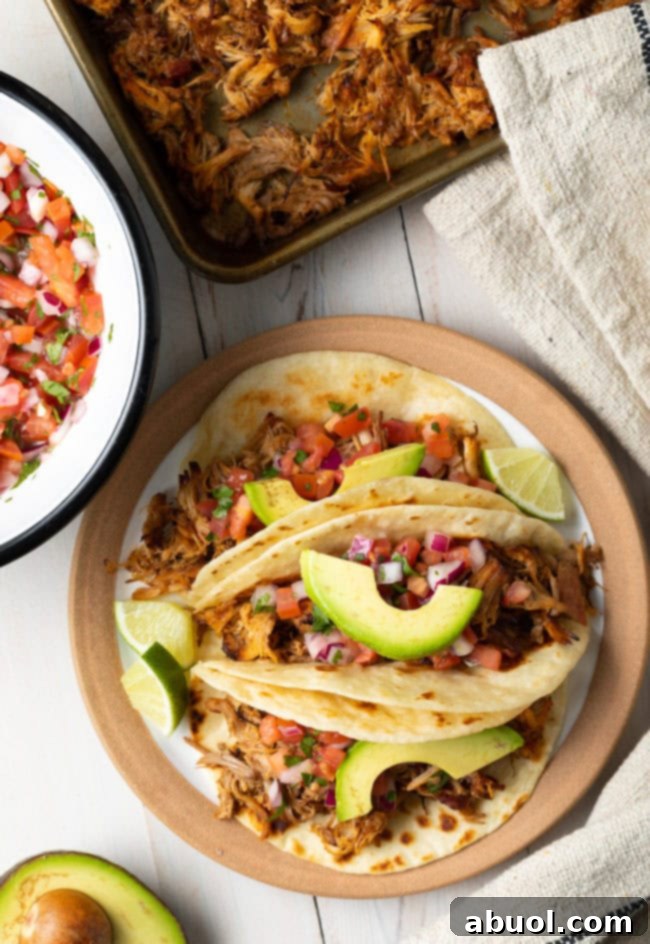 Overhead shot of plated slow cooker carnitas topped with fresh avocado slices and wedges of lime, ready to be served.