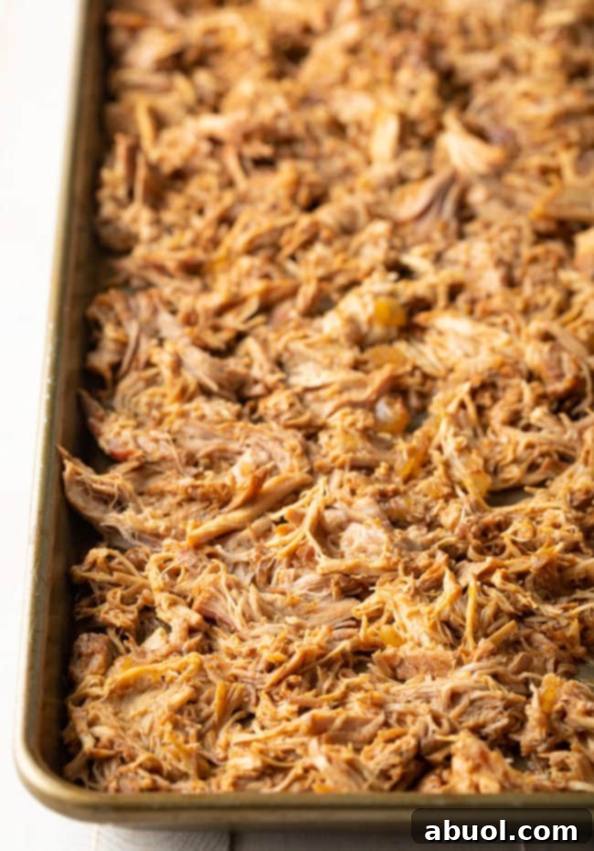 Shredded carnitas spread in a thin, even layer on a baking sheet for broiling.