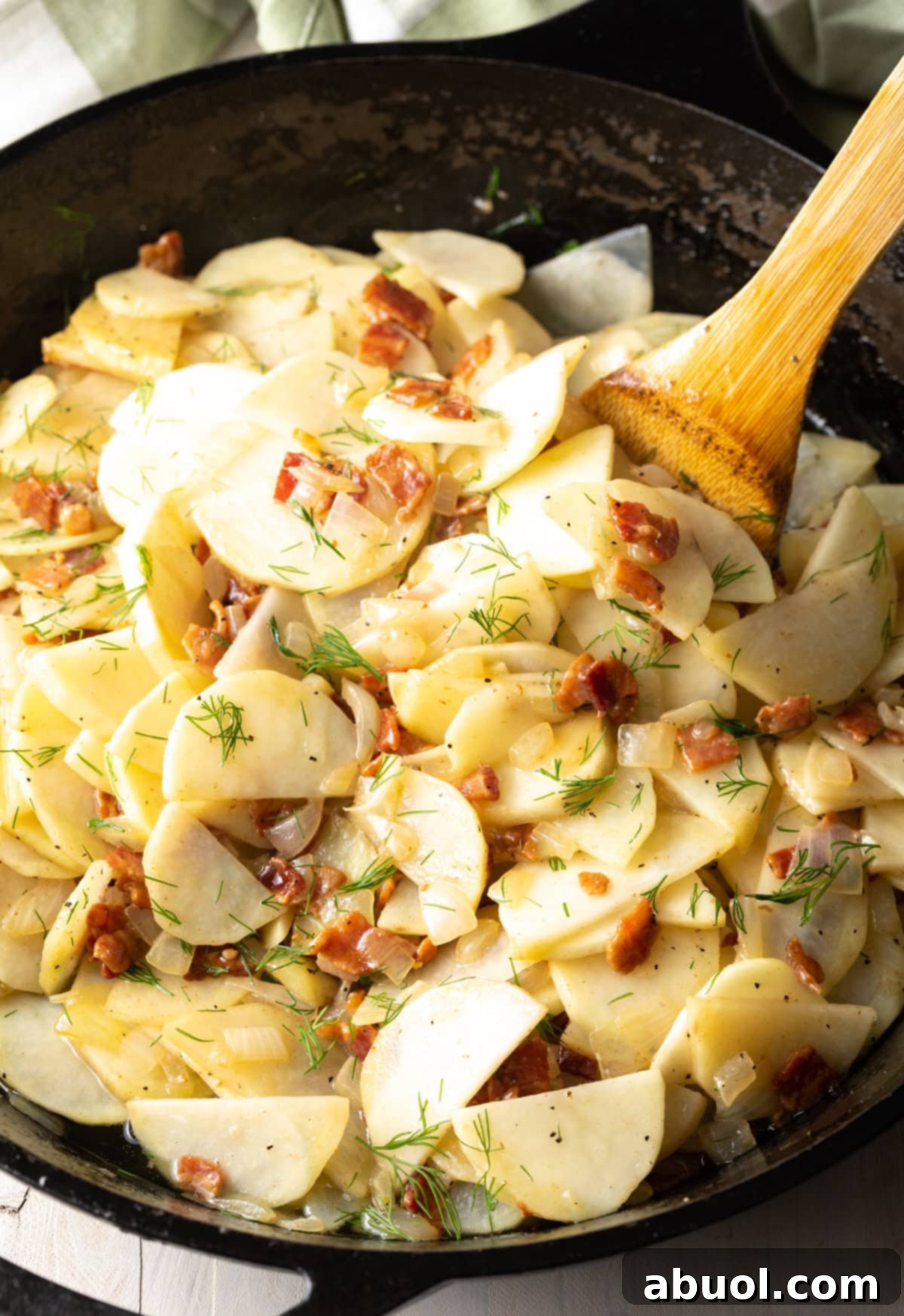 Potatoes, bacon, onions, and dill cooking together in a pan, coated in rich bacon grease.