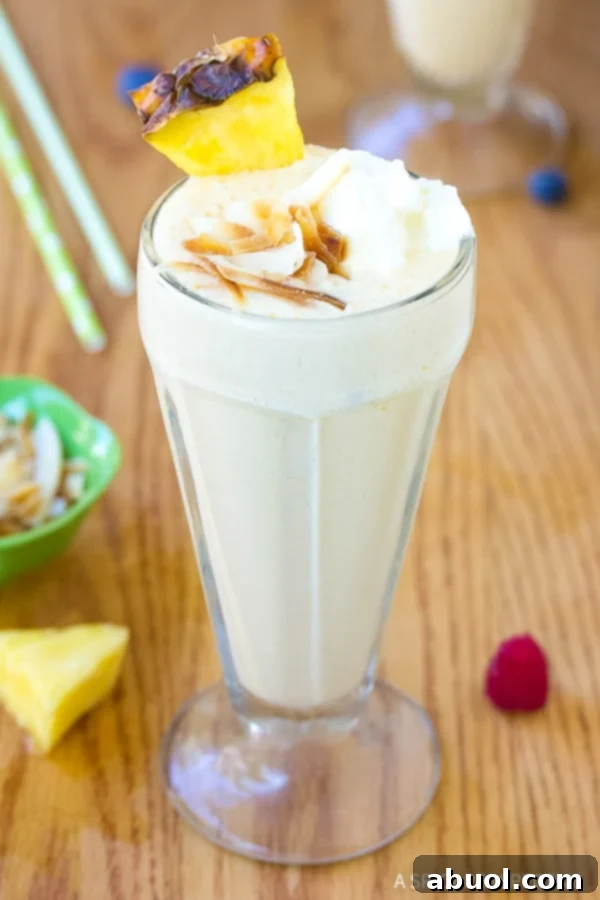 A tall glass filled with a pineapple milkshake and topped with toasted coconuts. 