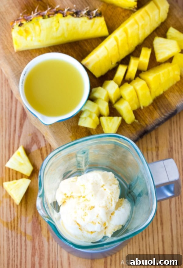 Blender loaded with ice cream and a cutting board topped with chopped pineapple and a jar full of pineapple juice. 