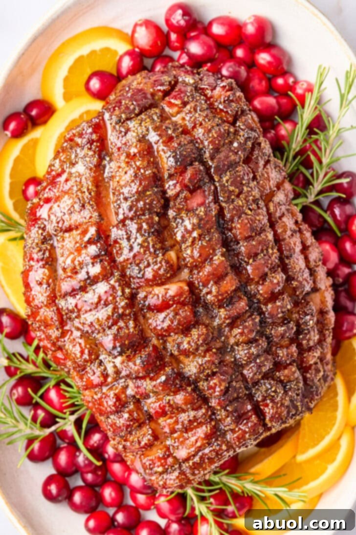 Overhead shot of a beautifully brown sugar glazed ham on a festive serving platter, garnished with fresh cranberries, orange slices, and fragrant rosemary sprigs.