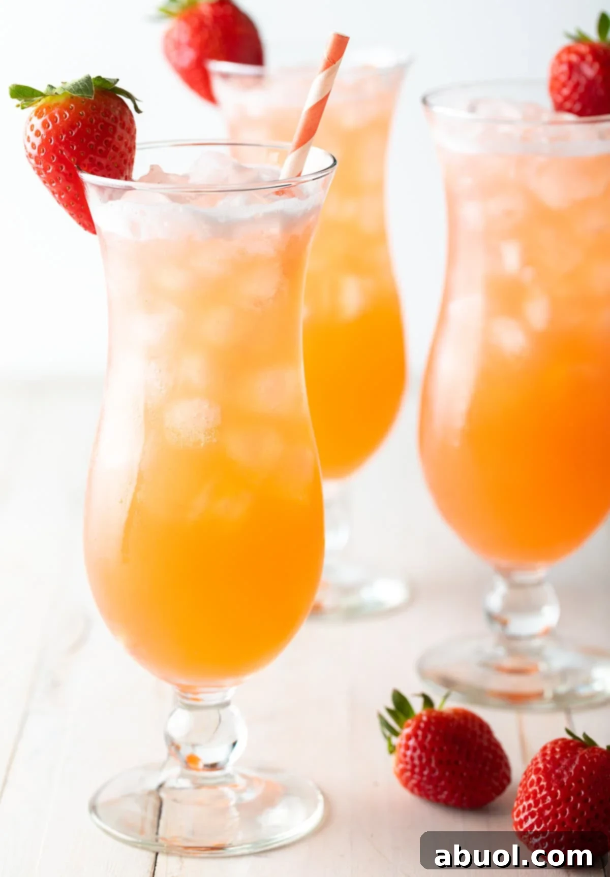 3 tall cocktail beverage glasses filled with strawberry pineapple agua fresca. Each glass is garnished with a strawberry on the rim and and orange and white striped paper straw.