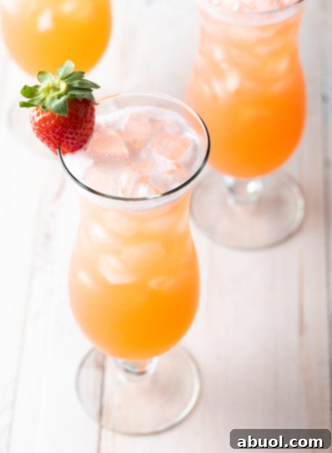 3 tall cocktail beverage glasses filled with strawberry pineapple agua fresca. Each class is garnished with a strawberry on the rim.