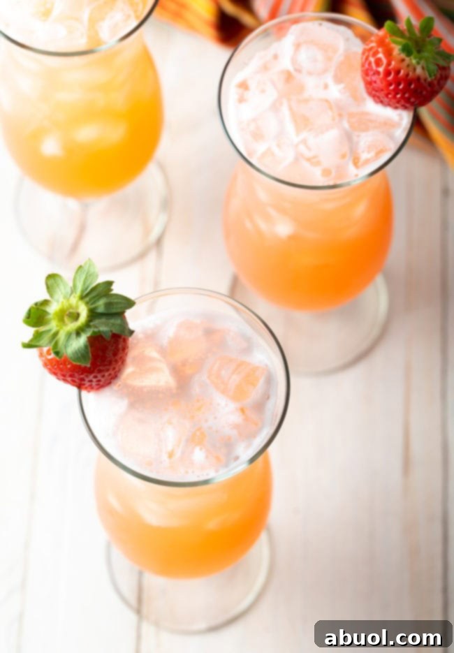 Top down view 3 tall hurricane glasses with authentic aguas frescas, each garnished with a whole strawberry.