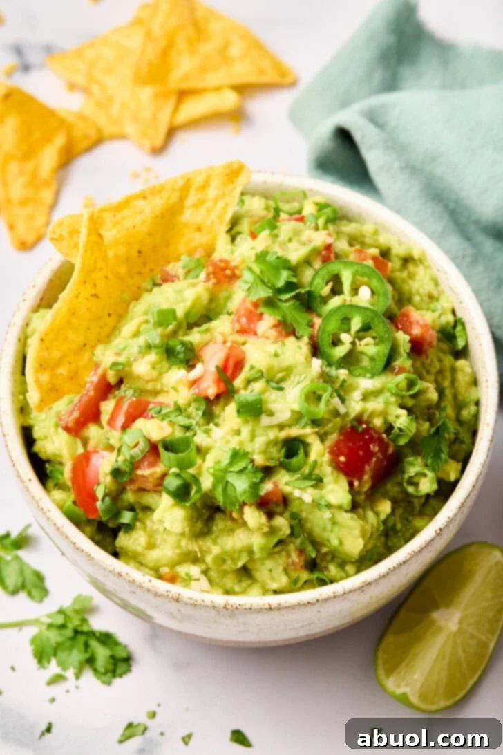 Guacamole-Recipe Guacamole topped with fresh ingredients in a white bowl with tortilla chips, ready to be served.
