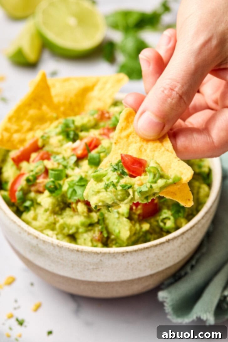 The Guacamole Gospel 12 A hand scooping up creamy guacamole with a crispy tortilla chip, capturing the perfect bite.