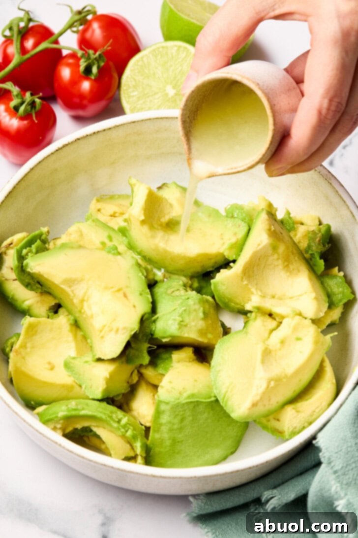 The Guacamole Gospel 5 Chopped avocados in a bowl with a hand pouring fresh lime juice over them to prevent browning.