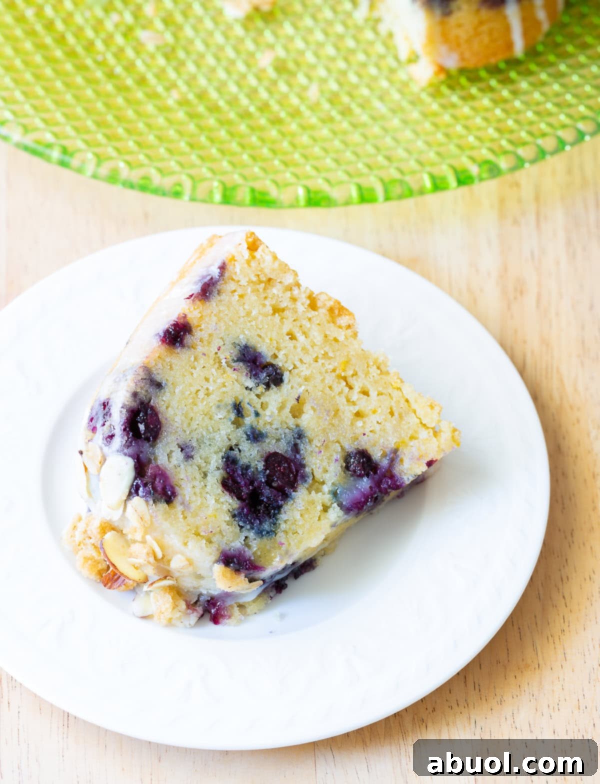 A mouthwatering slice of blueberry muffin bundt cake on a white plate, showcasing the berries and toppings.