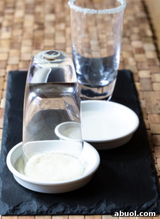 A close-up of a margarita glass being prepared with a salt rim, next to a pile of fresh limes.