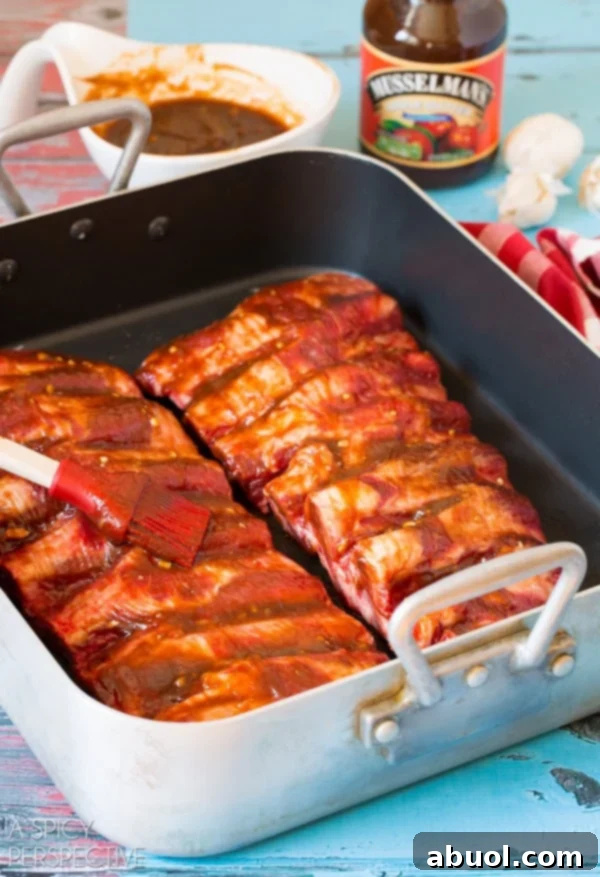 Beef ribs covered in cooking sauce sitting in baking pan with brush.