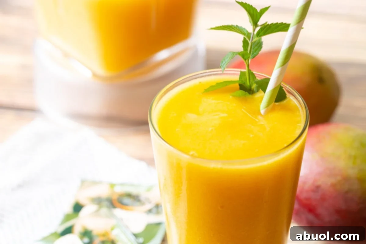 A refreshing Mango Green Tea Smoothie in a glass, garnished with a sprig of mint and a green and white straw, ready to be enjoyed.