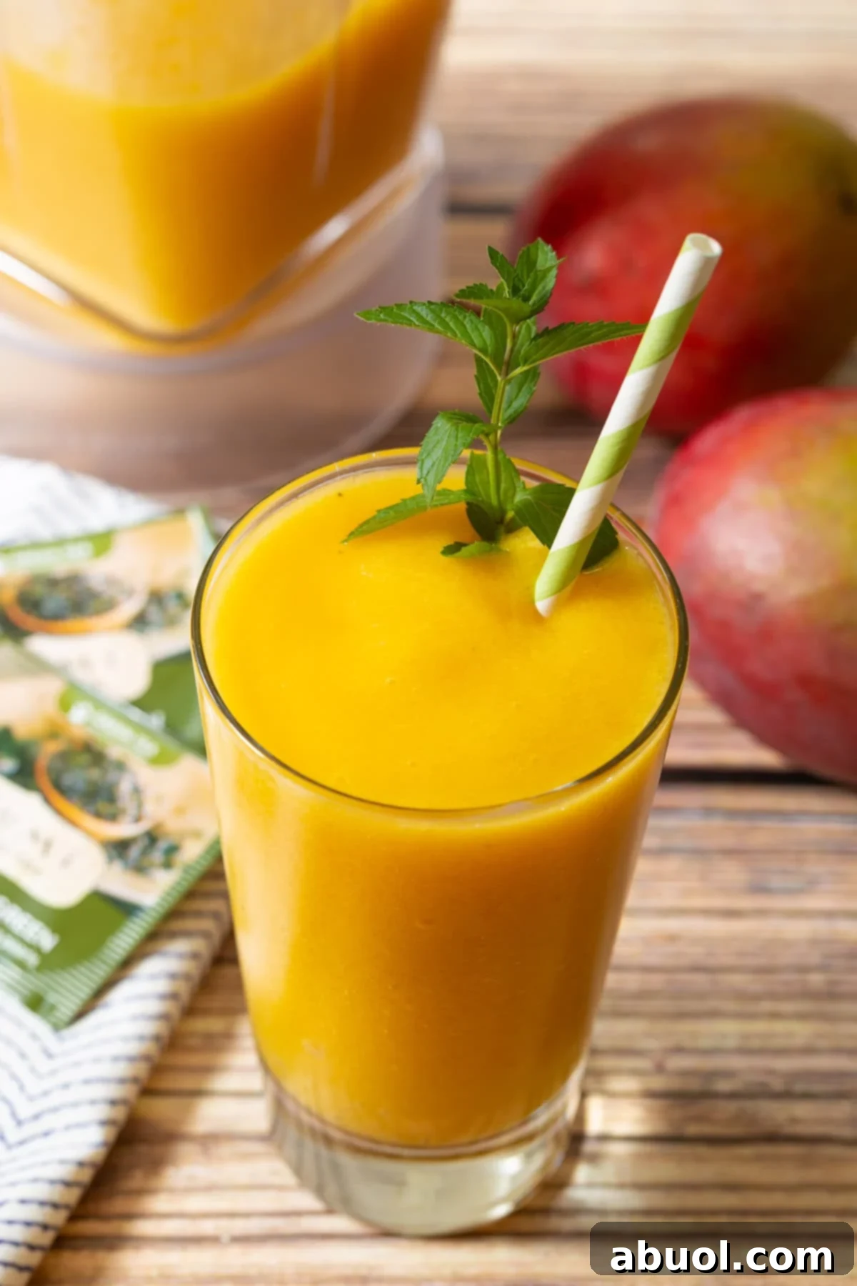 A close-up view of a full glass of Mango Green Tea Smoothie, garnished with mint and a green and white straw, highlighting its creamy texture and appealing color.