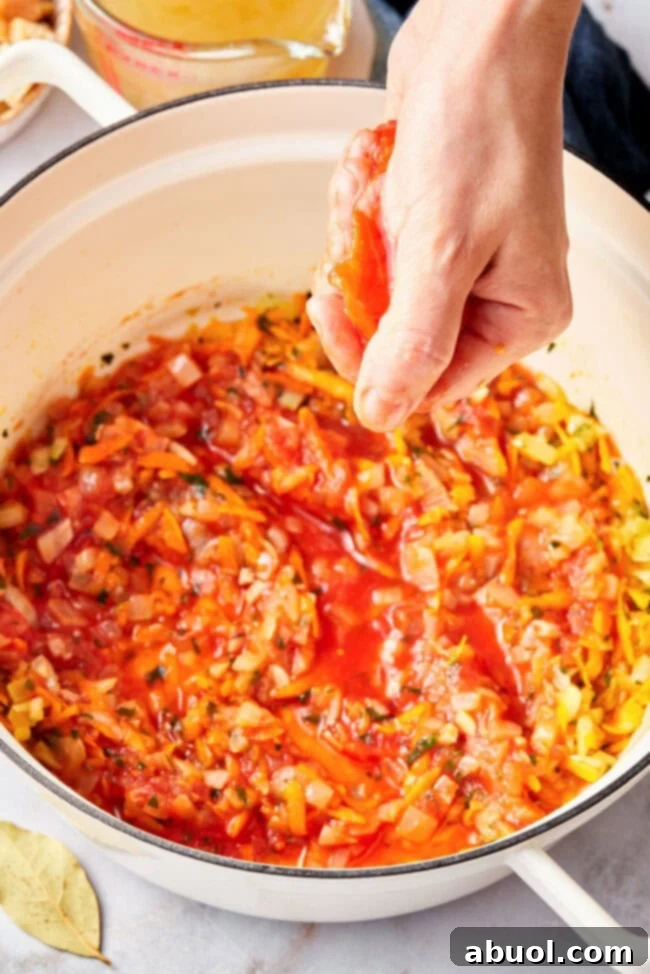 Hand squishing a whole San Marzano tomato before putting it in a pot to make tomato soup.