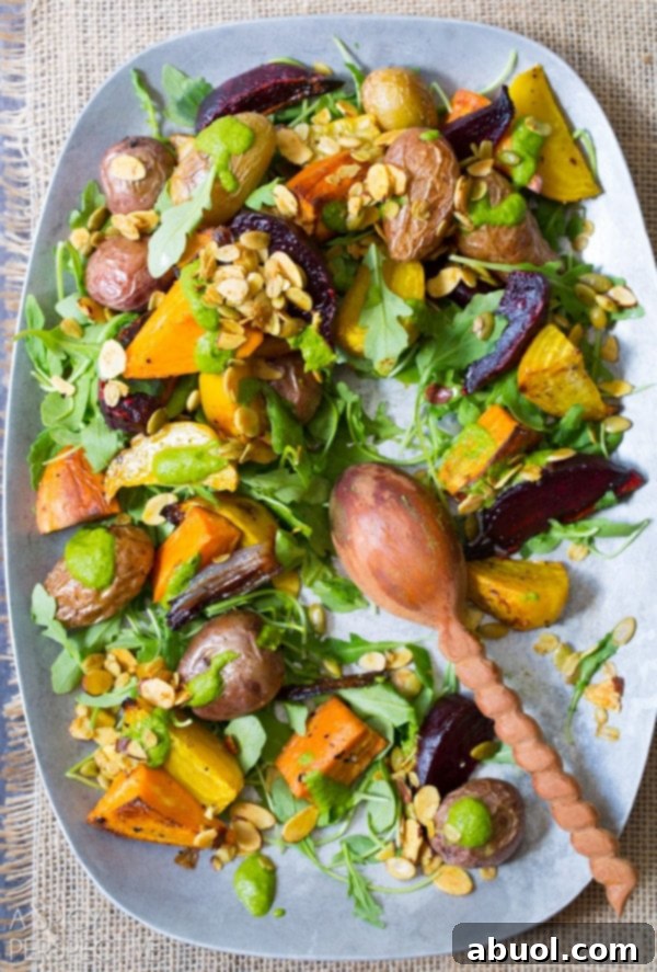 A top-down view of roasted vegetable salad on a large serving platter. A wooden spoon rests on the platter where a few servings have been taken, highlighting its appeal.