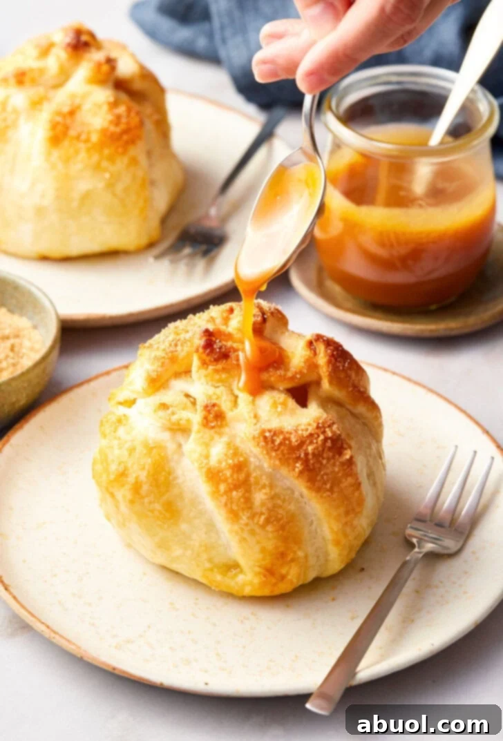 Finished mini apple pie bomb on a plate with caramel being drizzled on top with a spoon.