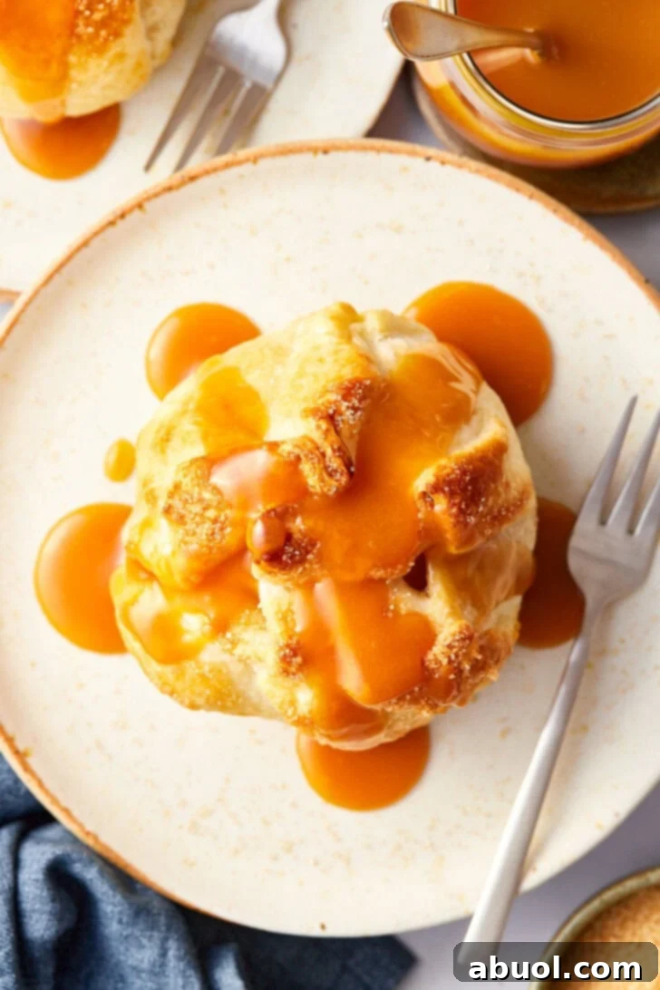 Baked apple wrapped in puff pastry on a plate with caramel drizzled on top. 