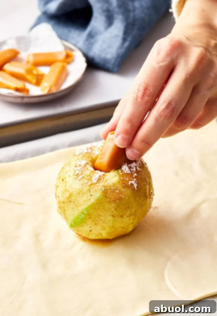 Peeled apple being stuffed with caramel candy for apple pie bombs.