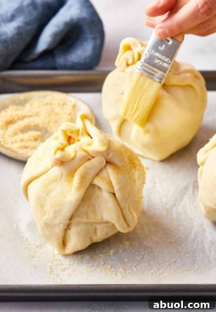 Un-baked puff pastry mini apple pie bombs with pastry brush brushing egg wash.