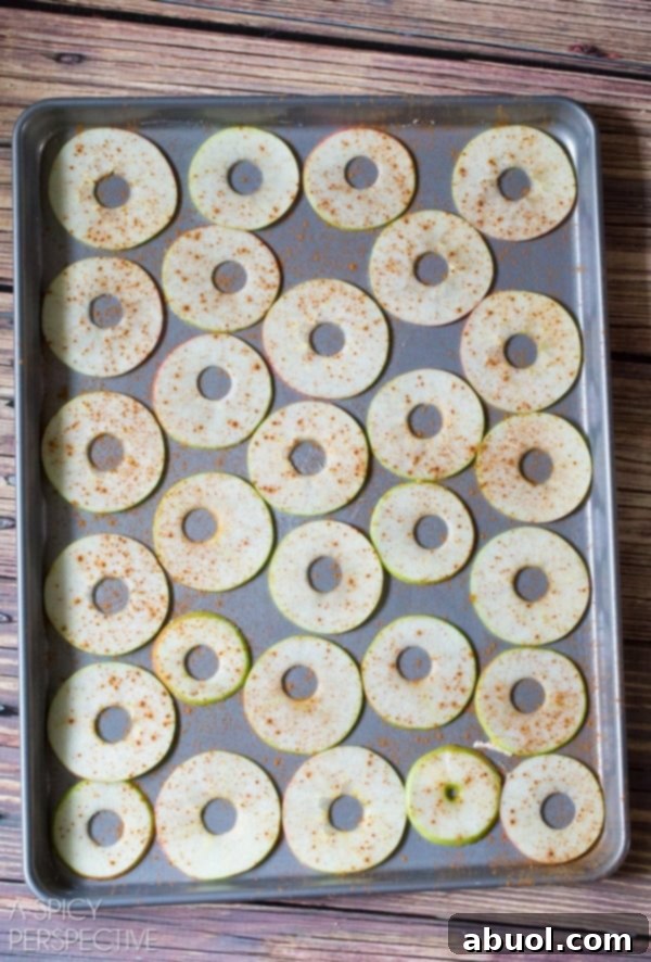 A top-down view of thinly sliced apples meticulously laid out in a single layer on a baking sheet, ready for baking.
