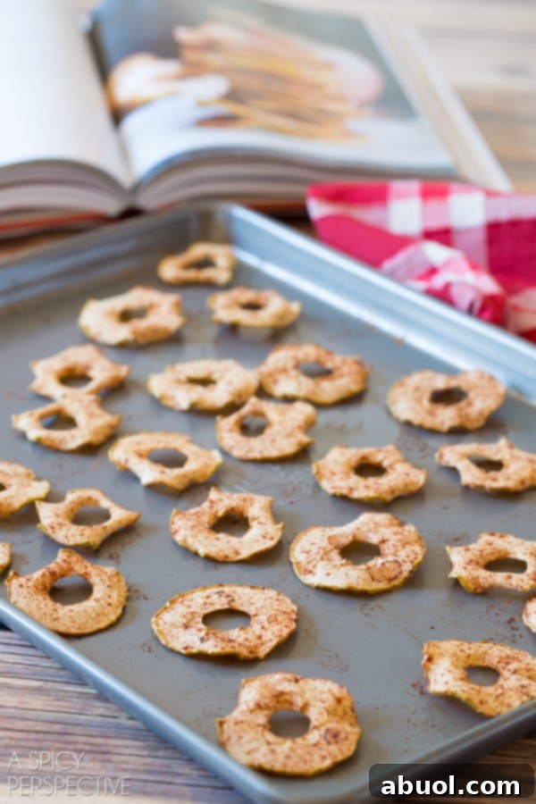 A close-up side view of golden-brown baked apple chips arranged neatly on a baking sheet, showcasing their crisp texture.