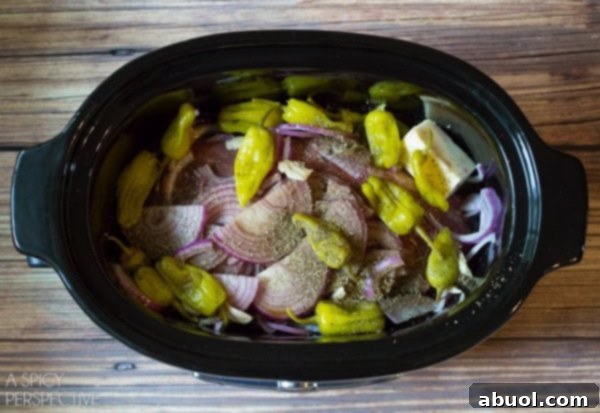 Close-up of raw ingredients for Slow Cooker Italian Beef, including beef roast, onions, garlic, and pepperoncinis.