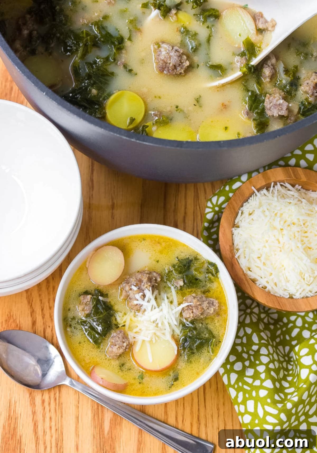 Parmesan Kale Soup - A white bowl with kale soup with a soup pot and wood bowl of parmesan cheese next to it.