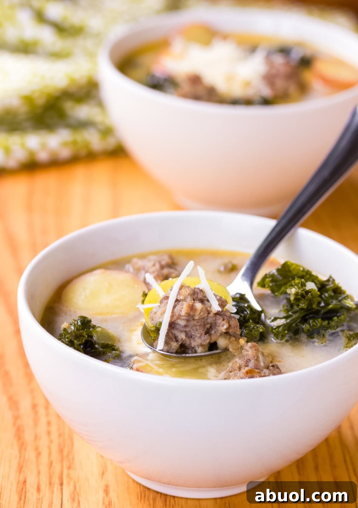 A side view of sausage and kale soup in a white bowl with a spoon.